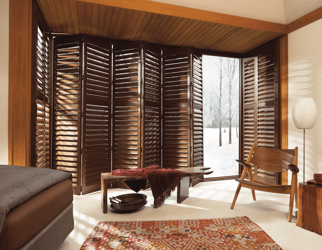 Bi-fold brown wood shutters on wide window in bedroom